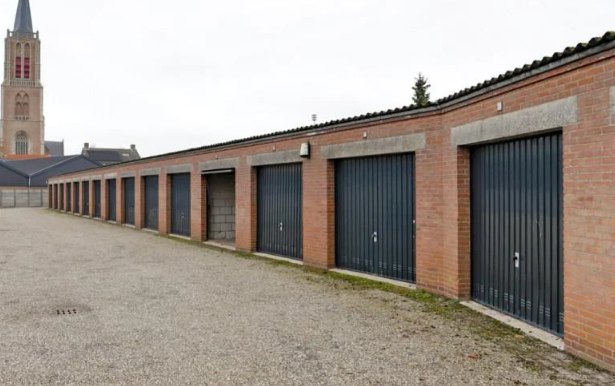 Lange rij bakstenen garageboxen met donkere kanteldeuren aan de Doelhof in Kloetinge, met de kerktoren op de achtergrond